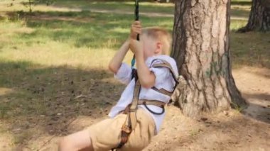 Ormandaki yaz kampında teleferiğe binen neşeli çocuğun portresi. Aktif çocukluk, sağlıklı yaşam tarzı, açık havada oynayan çocuklar, doğadaki çocuklar.