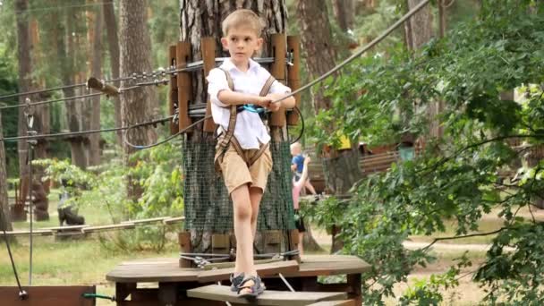 小さな男の子ぐらつきつり橋の上を歩いて夏のキャンプで2本の木の間にストレッチ キッズスポーツ 夏休み 屋外での楽しい スカウト — ストック動画