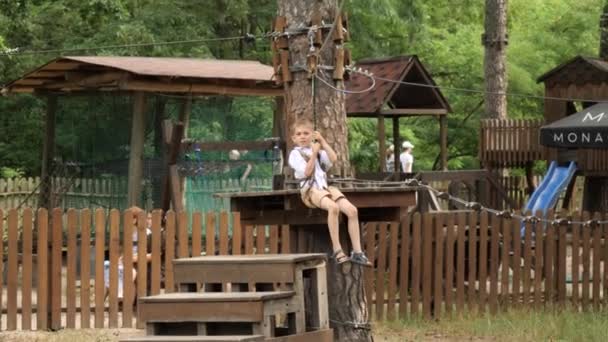 夏の公園でジップラインに乗っている間 小さな男の子は楽しんでいます キッズスポーツ 夏休み 屋外での楽しい スカウト — ストック動画