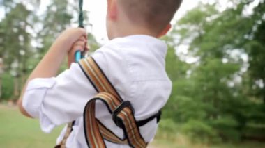 Neşeli gülen çocuk macera parkında iki ağacın arasında ip üzerinde geziyor. Çocuk sporları, yaz tatili, açık hava eğlencesi, izciler.
