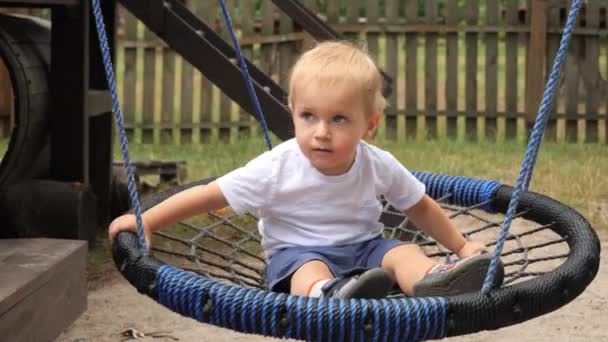 遊び場でロープネストスイングで揺れる幸せな笑顔の赤ちゃんの男の子 屋外で遊んでいる子供たち 楽しい夏休みを過ごしている子供たち — ストック動画