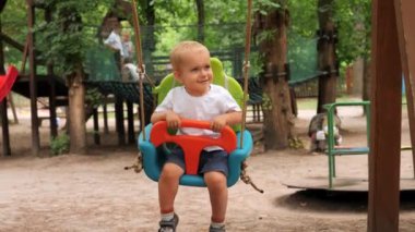 Mutlu gülümseyen oğlan renkli salıncakta sallanıyor. Çocuklar dışarıda oynuyor, çocuklar eğleniyor, yaz tatili ve tatil