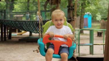 Parkta renkli salıncakta sallanarak eğlenen gülümseyen mutlu çocuğun ağır çekimleri. Çocuklar dışarıda oynuyor, çocuklar eğleniyor, yaz tatili ve tatil