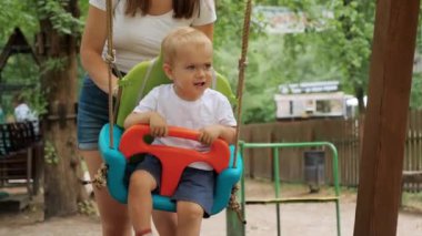 Annesi yaz parkında çocuk parkında sallanan mutlu bir çocuk. Çocuklar dışarıda oynuyor, çocuklar eğleniyor, yaz tatili ve tatil