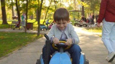Çocuklar için oyuncak traktör sürerken parkta eğlenen neşeli çocuğun portresi. Çocuklar parkta oynar, çiftçilik yapar, taşıma araçları kullanır..