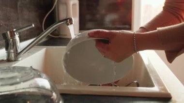 Lavaboda bulaşıkları süngerle yıkayan bir kadın. Ev hanımı çalışıyor, ev işleri yapıyor, ev işi yapıyor.