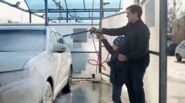 Oğlu olan genç bir baba oto yıkama servisinde araba yıkıyor. Ebeveynlik kavramı, ebeveynlere ve otomobil bakımına yardım eden çocuklar