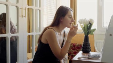 Zarif esmer kadın aynada yatak odasında oturuyor ve kırmızı ruj sürüyor. Cilt bakımı, kadın sağlığı ve güzelliği