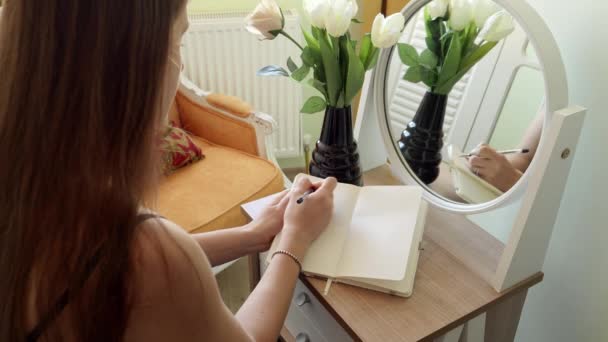 鏡で化粧台に腰掛けてノートに書く女の後ろ姿 女性の秘密 優雅さ — ストック動画