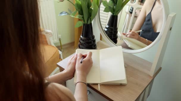 年轻女子的衣服坐在卧室的镜子前 用笔记本书写 女性秘密 — 图库视频影像