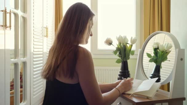 Zdjęcie Panningu Młodej Kobiety Siedzącej Biurkiem Obok Dużego Okna Zapisującej — Wideo stockowe