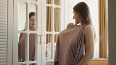 Aynaya poz veren ve giyecek elbise seçen güzel bir genç kadının portresi. Kıyafet seçimi, moda ve tarz kavramı