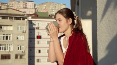 Sabahın erken saatlerinde ekose giyinmiş, balkonda kahve içen ve şehri seyreden gülümseyen kadın. İnsanlar rahatlıyor, evlerinde dinleniyor, güzel şehir manzarası