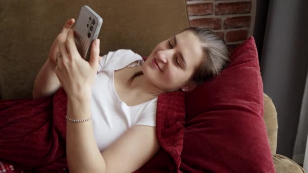 Femme Souriante Couchée Sur Canapé Naviguant Sur Internet Sur Smartphone — Video