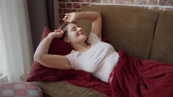 穿着睡衣的快乐微笑的女人躺在沙发上 伸出手来 妇女在家休息 生活方式和放松 — 图库视频影像