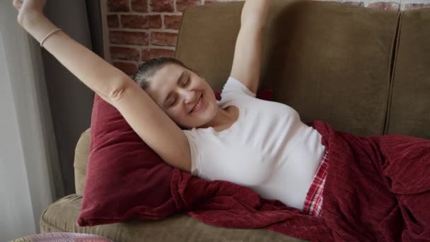 早上穿着睡衣的快乐微笑的女人躺在沙发上伸展的画像 妇女在家休息 生活方式和放松 — 图库视频影像
