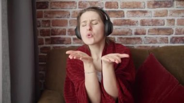 Kulaklık takıp evde dans eden aktif ve neşeli bir kadının portresi. İnsanlar evde rahatlıyor, eğleniyor, olumlu duygular ve sevinç yaşıyor.