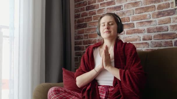 蓮のポーズで座ってヘッドフォンで瞑想する美しい女性 リラクゼーションの概念 健康的なライフスタイル 自宅で休んでヨガを練習 — ストック動画