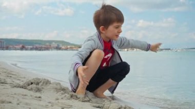 Çocuk deniz sahilinde oturuyor, kazıyor ve kumla oynuyor. Turizm, seyahat, yaz tatili ve hafta sonları kavramı.