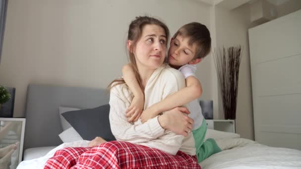 若い思いやりと愛情の少年は動揺した母親がベッドの上に座って抱擁 愛の家庭 父母と子女 愛と支援の概念 — ストック動画