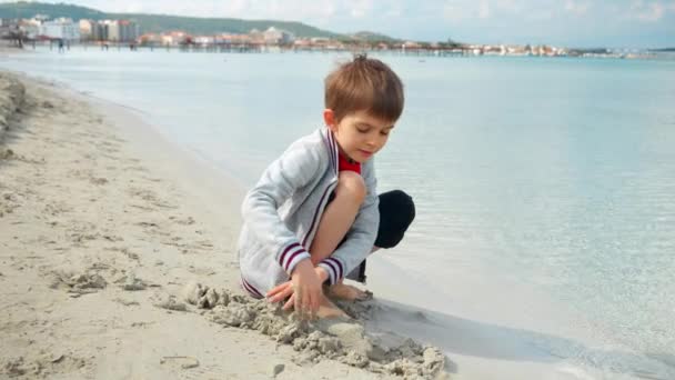 Młody Chłopiec Siedzi Słonecznej Plaży Kopiąc Rękami Ciepły Piasek Ciesząc — Wideo stockowe