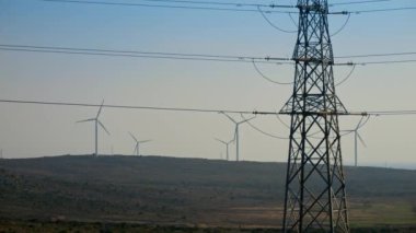 Dönen rüzgar türbinleri ve yüksek voltajlı elektrik hatları olan bir vadi. Yeşil elektrik kavramı, yenilenebilir enerji ve modern teknolojiler.