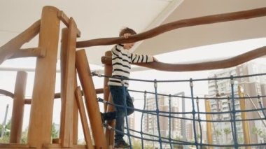Parktaki oyun parkında tahta ip köprüde dengede duran küçük çocuk..