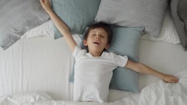 Sevimli küçük çocuk yatakta uzanıyor, ellerini uzatıyor ve esniyor. Çocuk sabah yataktan kalkıyor.