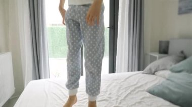 Sabahları büyük pencerenin önünde pijamalı, yatakta zıplayan neşeli çocuğun yavaş hareketi. Mutlu çocukluk, eğlence ve neşe