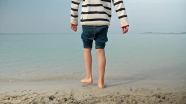 Küçük çocuk denizde yürüyor ve sakin turkuaz okyanus dalgalarına bakıyor. Tatil, tatil, doğada hafta sonu.