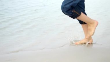 Kumlu deniz sahillerinde koşan ve su sıçratan çocuk ayaklarının yavaş çekimleri. Tatil, tatil, doğada hafta sonu.
