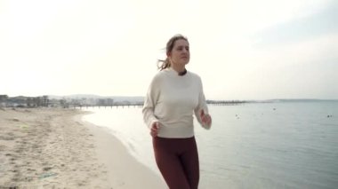 Gün batımında su yüzeyinde ve kumda kumlu sahilde koşan bir kadının sağlıklı ve zinde kalması ağır çekim.