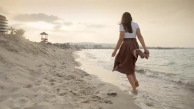 Kumsalda koşan genç bir kadının yavaş çekimde yalınayak ve tasasız ayak parmaklarının arasındaki sıcak kumu hissederek koşması. Farkındalık, seyahat ve tatil kavramı