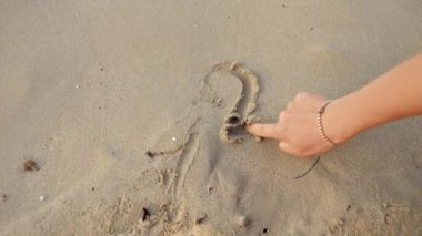Kadın elinin parmaklarıyla 2023 'ü okyanus sahilindeki ıslak kumda yazarken yakın plan fotoğrafı..
