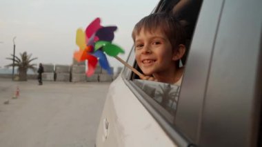 Gün batımını seyrederken renkli fırıldak tutan neşeli çocuğun portresi açık araba penceresinden.