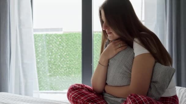 ベッドの上に座ってしっかりとクッションを抱いているパジャマ姿の思慮深い若い女性を動揺させます うつ病 負の感情 孤独とストレスの概念 — ストック動画
