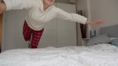 Yavaş hareket eden neşeli kadın yumuşak yatakta zıplar ve uçar. Evde rahatlama, mutluluk ve eğlence kavramı.