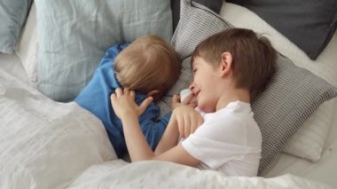 Yumuşak yastıklarda uzanmış birbirine gülümseyen iki tatlı çocuk. Mutlu çocukluk kavramı, evde eğlence ve neşeli çocuklar.