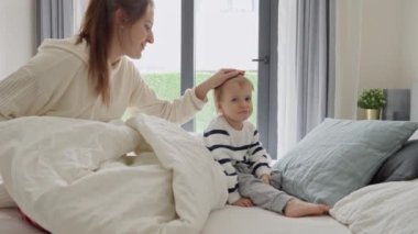 Genç anne üzgün oğlunu okşuyor ve sakinleştiriyor. Yatakta yatıyor.