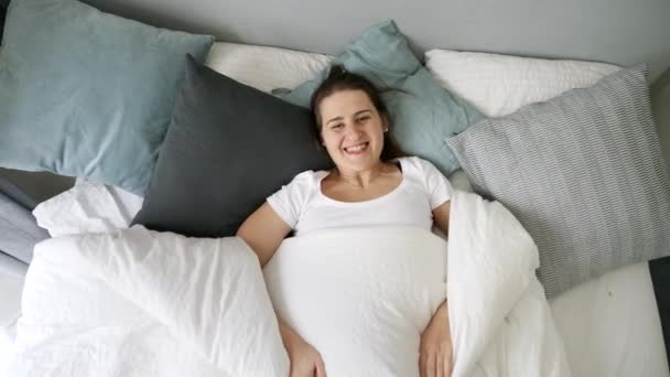 年轻的女人躺在床上 躺在毯子下 打开毯子 对着镜头微笑 家庭快乐 周末放松 早上快乐的概念 — 图库视频影像