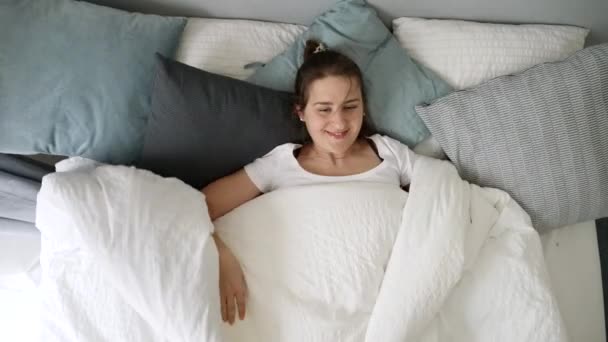 Молодая Женщина Лежит Постели Бросает Одеяло Смотрит Окно Улыбкой Лице — стоковое видео