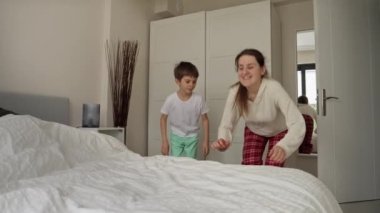 Gülümseyen oğlu yumuşak yatakta koşup zıplayan mutlu bir anne. Aile mutluluğu kavramı, evde dinlenmek, yatakta eğlenmek, ebeveynler ve neşeli çocuklar..