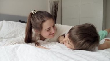 Sevgi dolu bir annenin portresi. Oğluyla yatakta pijamalarıyla uzanmış ve ona sarılıyor. Mutlu aile kavramı, çocuklu ebeveynler, olumlu duygular ve evde rahatlama.