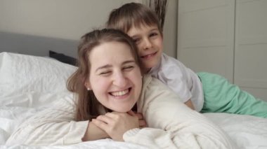 Mutlu neşeli çocuk, annesiyle yatakta uzanıyor ve ona sarılıyor. Mutlu aile kavramı, çocuklu ebeveynler, olumlu duygular ve evde rahatlama.