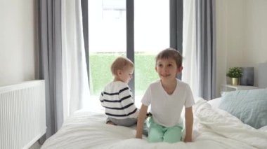 Sabahları pijamalı iki neşeli çocuk büyük yatakta zıplıyor. Mutlu aile kavramı, olumlu duygular ve evde rahatlama.