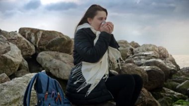 Genç bir kadın, kışın deniz kenarında sıcak giysiler içinde ve elinde sıcak çay termosuyla keyif çatıyor. Reklamlarda, tanıtım materyallerinde ya da seyahat videolarında kullanmak için mükemmel.