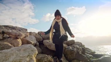 Sırt çantalı genç bir kadın deniz kıyısındaki kayalık kayalıklarda kış yürüyüşü yapıyor. Bir kış yolculuğu ve açık hava macerası konsepti..
