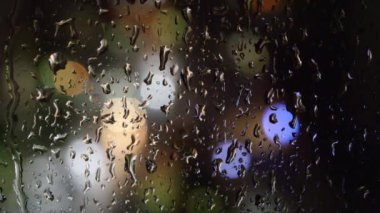 Geceleri pencereden süzülen yağmur damlaları ve akarsular. Arkaplanda renkli bokeh ışıkları
