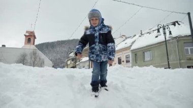 Gülümseyen mutlu çocuk sokakta oynayıp büyük bir kar yığınında zıplıyor. Neşeli bebek, kışın oynayan çocuklar, Noel tatilleri