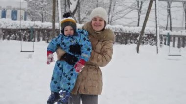Minik oğlunu kucağında tutan mutlu bir annenin portresi ve kar fırtınasından sonra çocuk parkında kar yığınlarının üzerinde yürümesi. Kış tatillerinde eğlence ve neşe, dışarıda oynayan çocuklar, kar yağışında faaliyet
